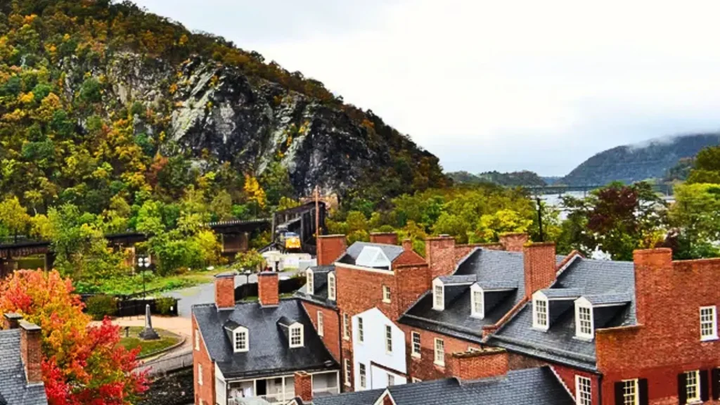 Harpers Ferry's historic Lower Town in the fall. The red brick and fall foliage contrast with the black wet roofs below the rocky and densely forested hill.