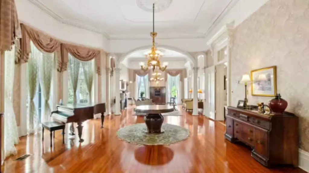 The interior of the Bucker Mansion, which is currently is not open to the public. It's very white with beige, curtains, chandeliers, a vintage piano, side chests, tables, and other furniture with wooden floors that shine.