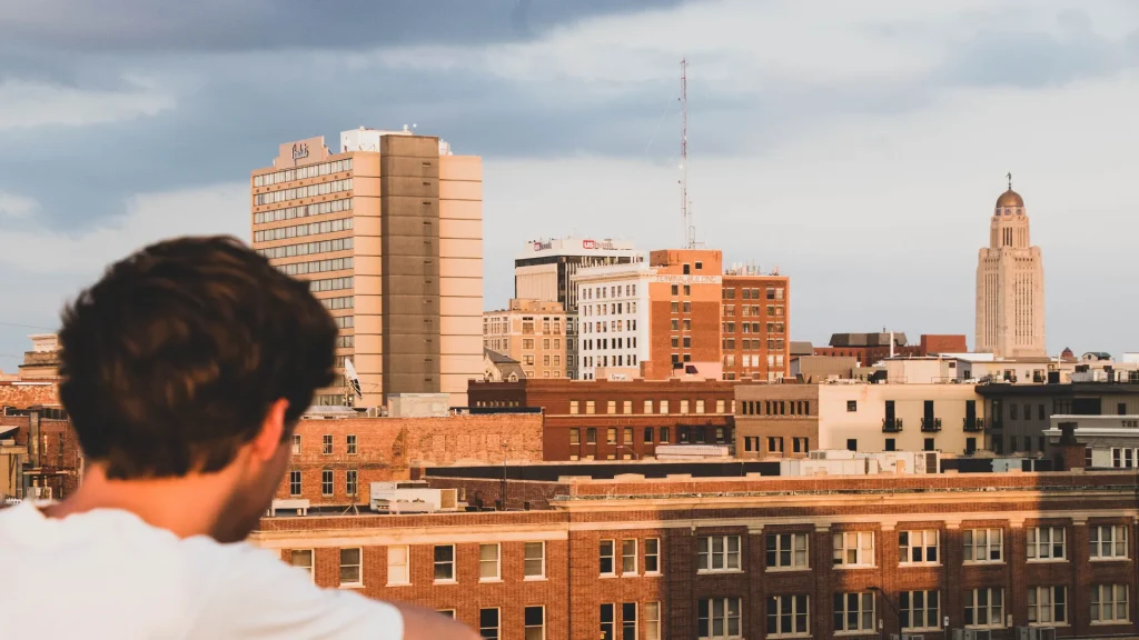 A boy in a white tee looking out at the Lincoln, NE skyline on an overcast day.