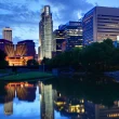 An image of the Lincoln, NE, skyline at night as lights reflect in the water below.