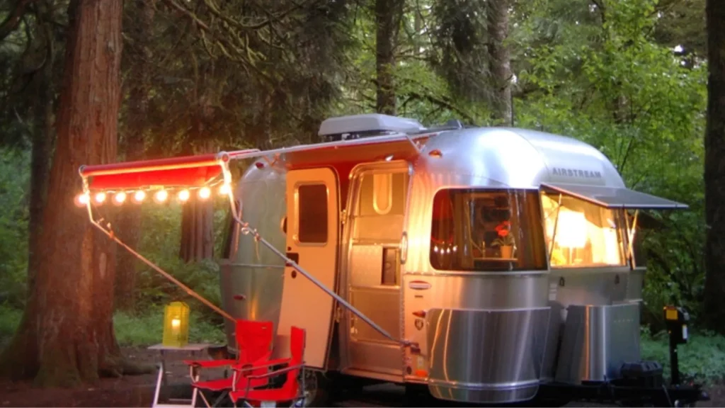Milo McIver's campground features 44 electric sites with full hookups and 9 primitive tent sites. This photo shows an airstream camper set up with lights and a patio area. 