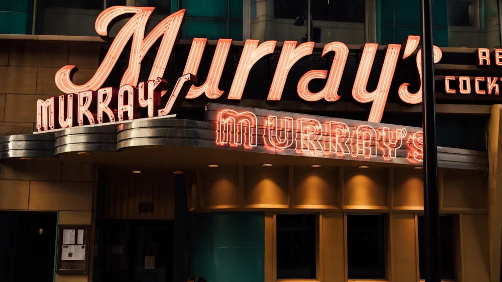 The exterior of Murray's and its neon sign. The sign is red and is styled after a 1950s mid-century modern style. 
