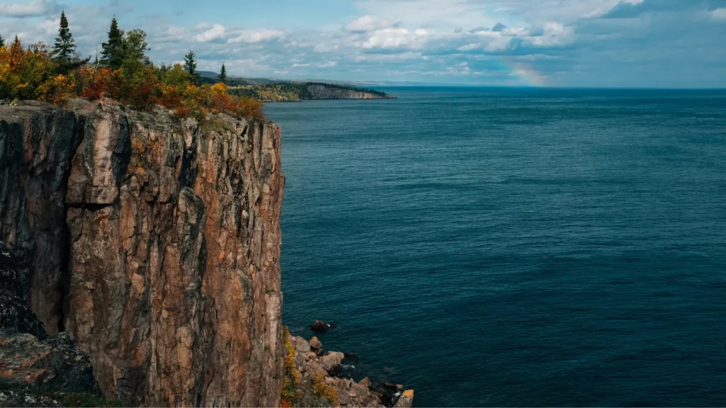 Palisade Head in Minnesota. The top of the craggy rust-colored cliff is full of fall-toned foliage. 