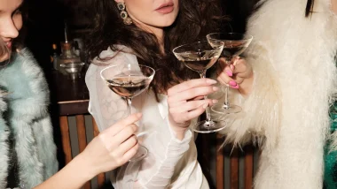 Three women stand around together, toasting with champagne glasses.