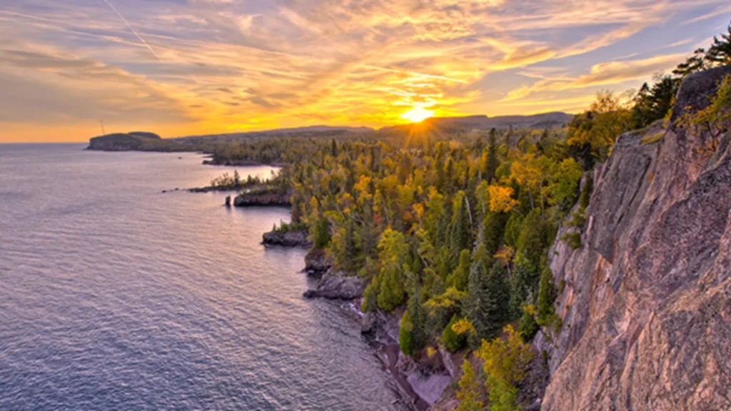 An aerial photograph of Tettegouche State Park at sunset. The golden light shines atop the park, highlighting the yellow tones in the trees. 