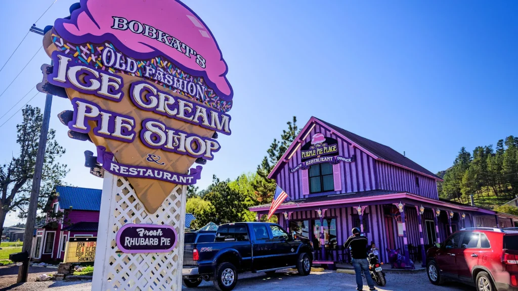 The Purple Pie Place and it's ice cream sign outside duirng a sunny day as people park and stand outside to enter the building. 