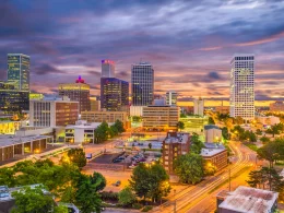 Downtown Tulsa, OK, at night with a cloudy, dark sky. The city lights luminate the city.