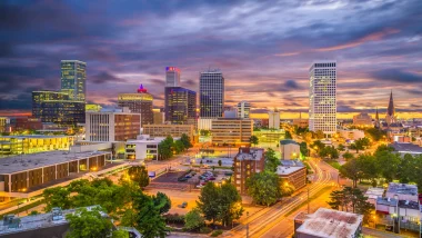 Downtown Tulsa, OK, at night with a cloudy, dark sky. The city lights luminate the city.