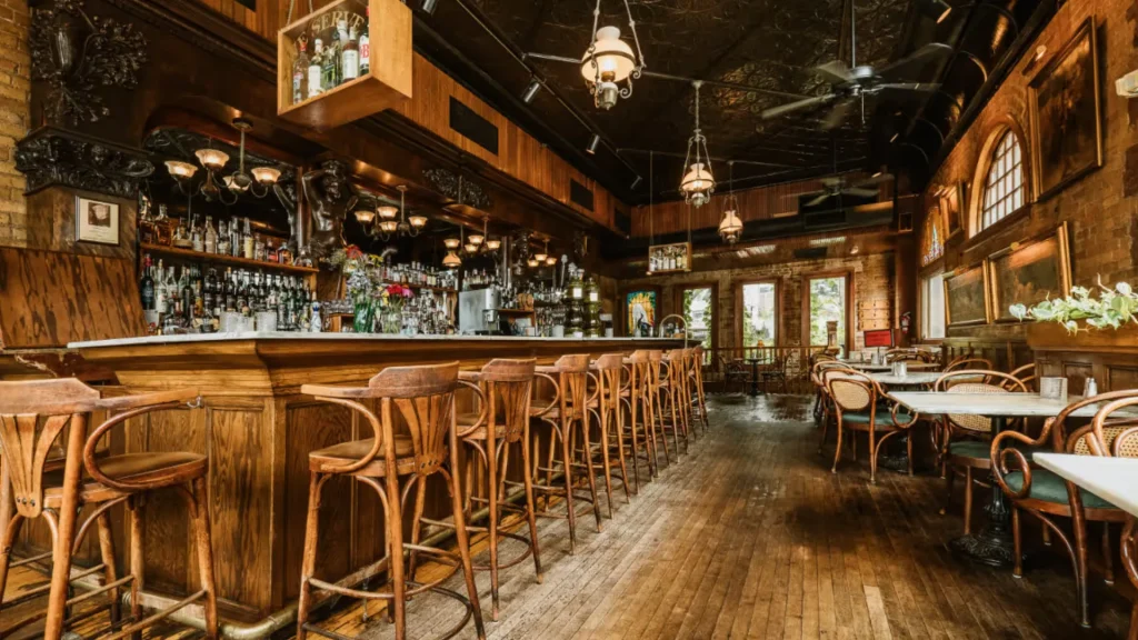 The interior of W.A. Frost & Company and its bar. It's mostly wood with wooden floors, chairs, bar stools, and wood paneling up the wall. 