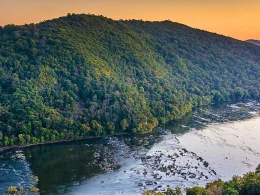 The sunset view from an outlook on the Weverton Cliffs hike. The sky is a citrus orange, which contrasts with the deep green and blue tones of the forested range.