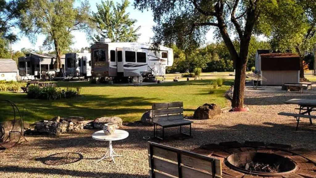 A fire pit and RVS at the Chillicothe RV and Recreation Area during the day. The fire pit is surrounded by gravel as the landscaping transitions into grass.