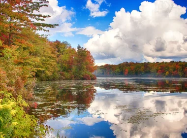 Tobyhanna State Park in the fall. The photo depicts a lake surrounded by fall colored foliage on a sunny yet cloudy fall day.