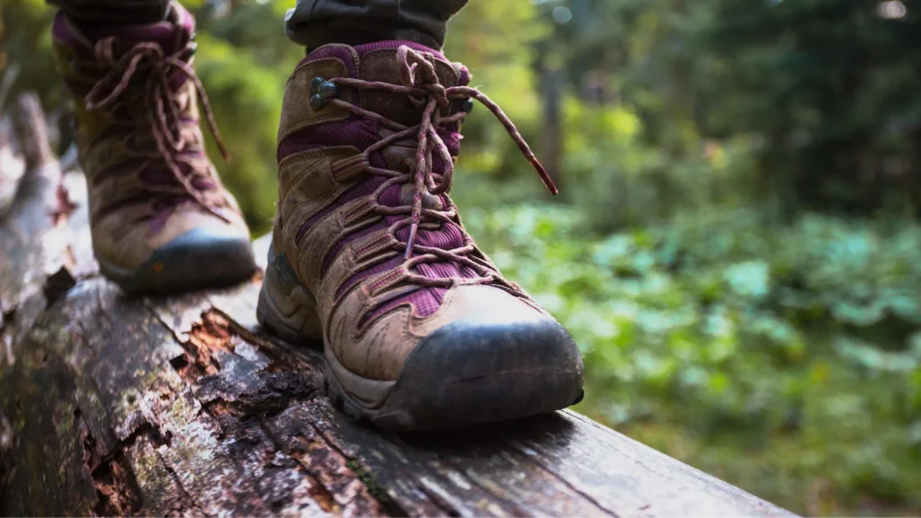 An up-close photo of a person wearing hiking boots with the boots walking on a log and a blurred green background.