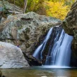 A photo of the Kilgore Falls as the light peeks through the fall colored trees.