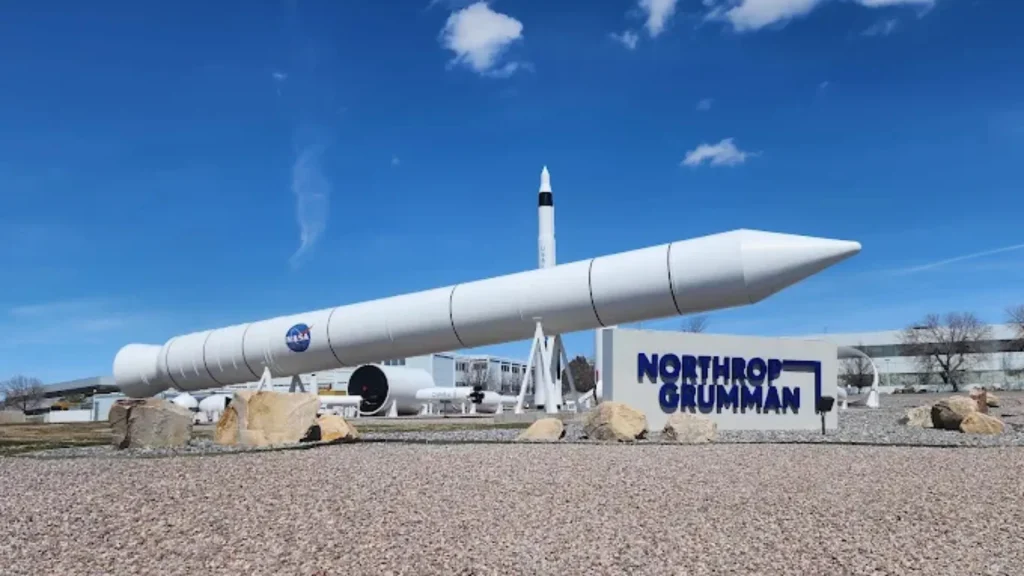 ATK Rocket Garden in Corinne, UT. The sky is bright blue above a large rocket with a sign in front of it saying: "Northrop Grumman". A NASA logo is on the side of the rocket.