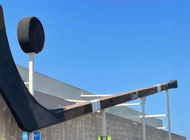 The Duncan Stick in B.C., Canada sits attached to a building with a bright blue sky behind it.