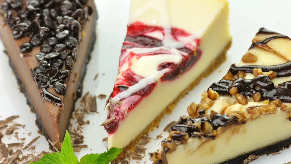 Three different slices of cheesecakes sit side by side in an arc formation with shaved chocolate and crust crumbs dispersed on the plate they sit on.