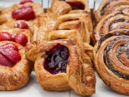 Three rows of baked pastries in a case on white parchment paper with various different fillings.
