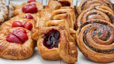 Three rows of baked pastries in a case on white parchment paper with various different fillings.