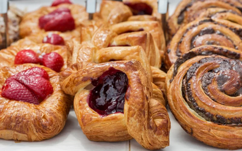 Three rows of baked pastries in a case on white parchment paper with various different fillings.