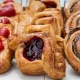 Three rows of baked pastries in a case on white parchment paper with various different fillings.