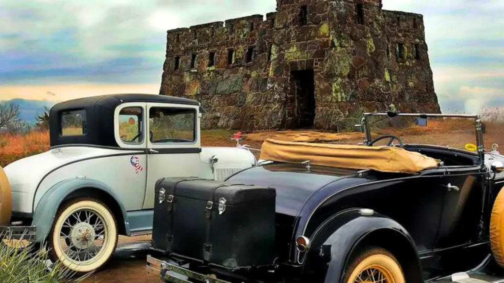 Two vintage vehicles are parked in front of the Coronado Castle on a cloudy day.