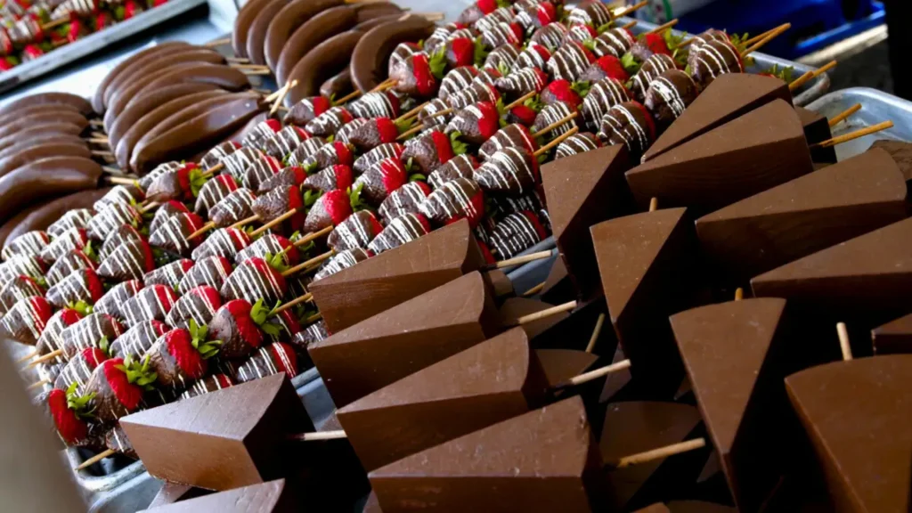A close-up photo from Chocolate Fest in Long Grove of chocolate-covered bananas, strawberries, and cheesecake all on skewers or popsicle sticks.