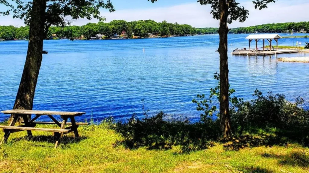 The Cordry and Sweetwater lakes in Indiana. Supposedly the cleanest lakes in the state. The images is of the lake, a bright blue color as we look out onto it from in front of a picnic table and two trees. 