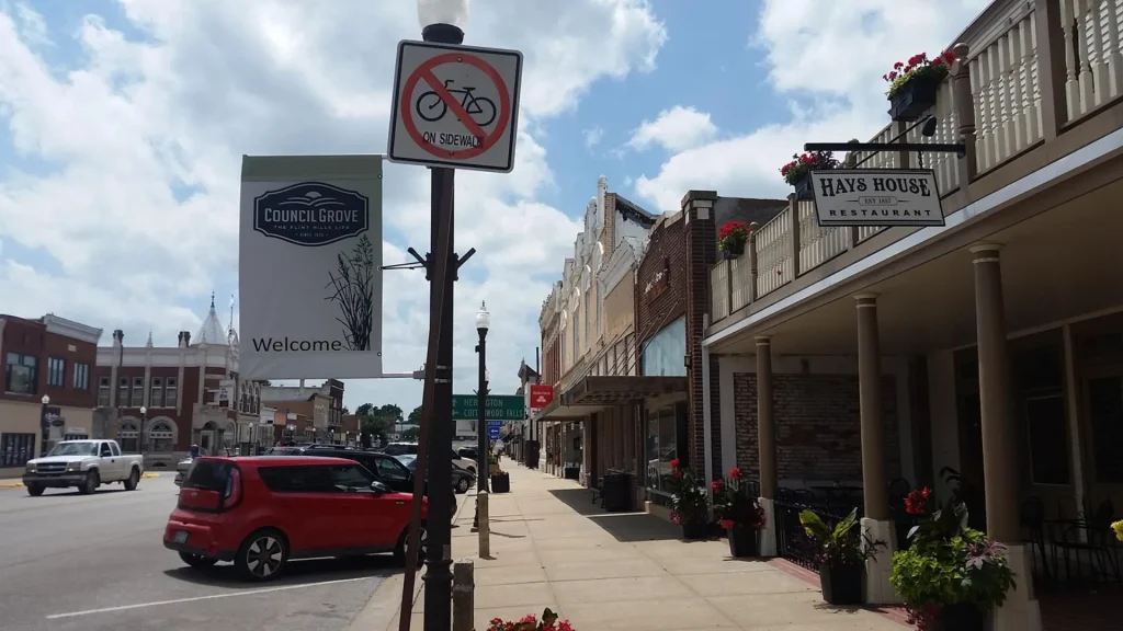 A photo of downtown Council Grove with shops lines store fronts lining the street as cars park on the road.