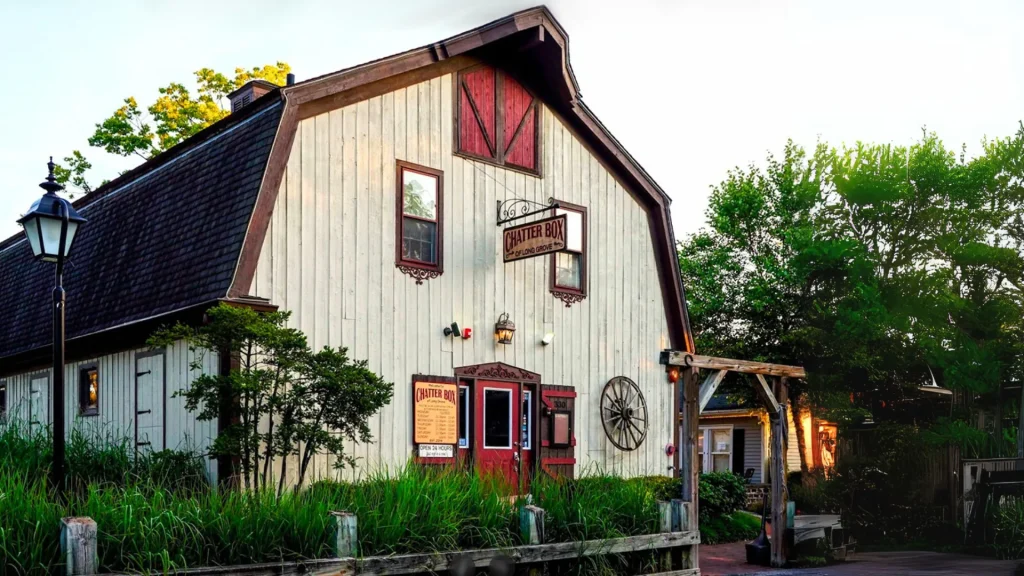 The restaurant Chatterbox in Long Grove, IL, is what looks to be a barn from the exterior with a wooden sign hanging from a decorative iron sign hanger and a red front door. 