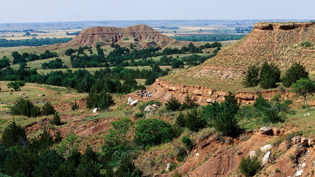 The Gypsum Hills in an aerial photograph showcasing the stunning red and orange rocky landscape. A group of horse riders trek up and around one of the hills.