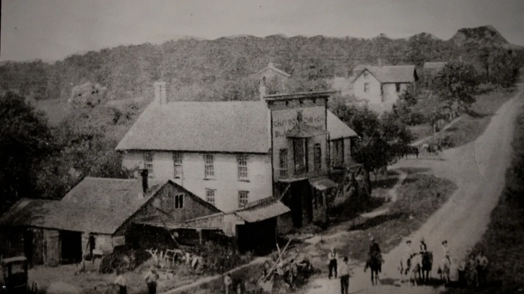 A historical photo of Long Grove depicts old buildings, people on horses, and a dirt road. The photo is grainy and black and white. 
