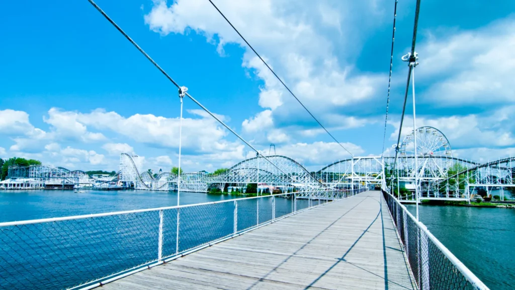 A bridge over a lake to a theme park with a bright blue sky being reflected into the water. 