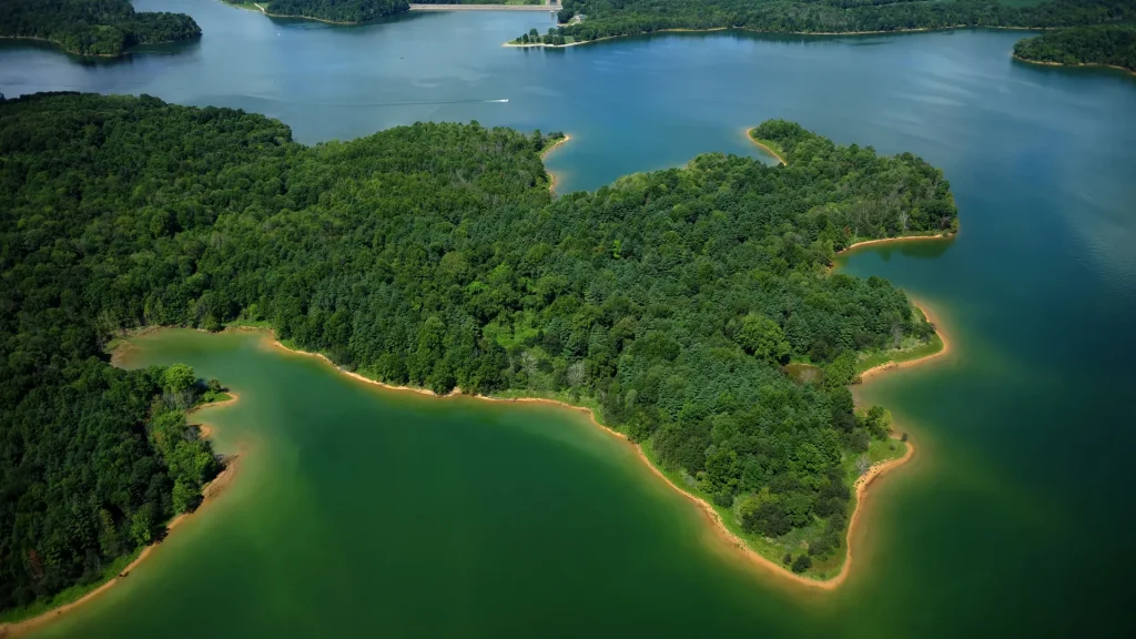 An aerial of Patoka Lake in Indiana. The water is a deep emerald, almost turquoise color as it wraps around an inlet or island, dense with trees. 