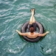 A person floating in a black inner tube atop clear blue water.