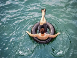 A person floating in a black inner tube atop clear blue water.