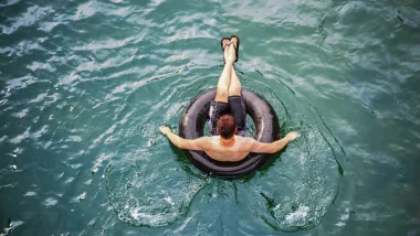 A person floating in a black inner tube atop clear blue water.