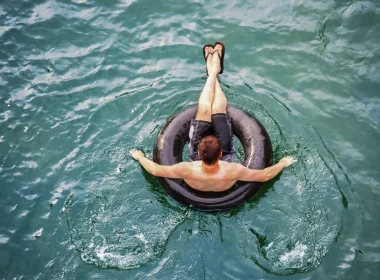 A person floating in a black inner tube atop clear blue water.