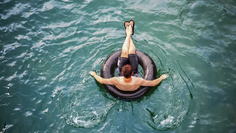 A person floating in a black inner tube atop clear blue water.