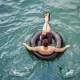 A person floating in a black inner tube atop clear blue water.