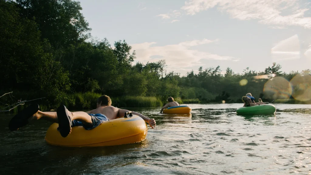 Three people in separate tubes floating atop the water that is surrounded by dense foliage.